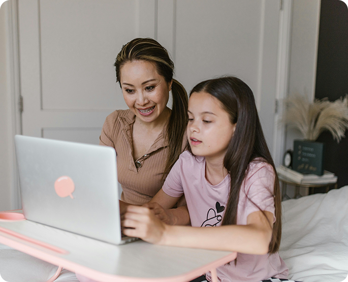 A woman and girl sitting at a table looking at a laptop.