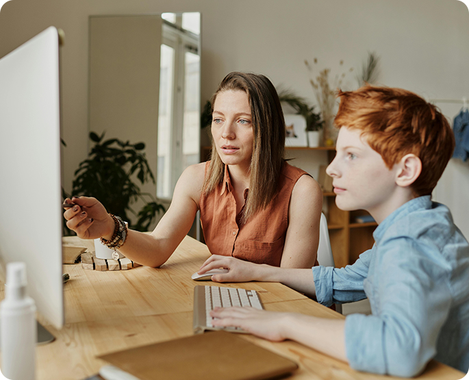 A woman and boy sitting at a table with a computer.