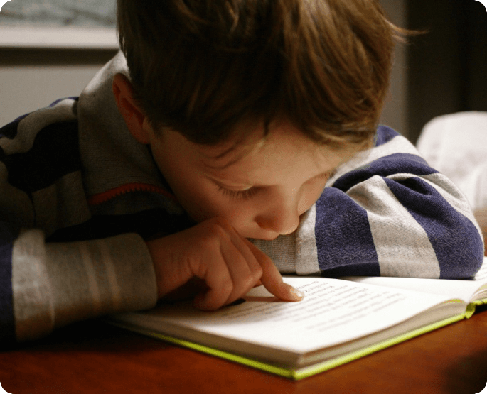 A young boy is reading a book on the table.