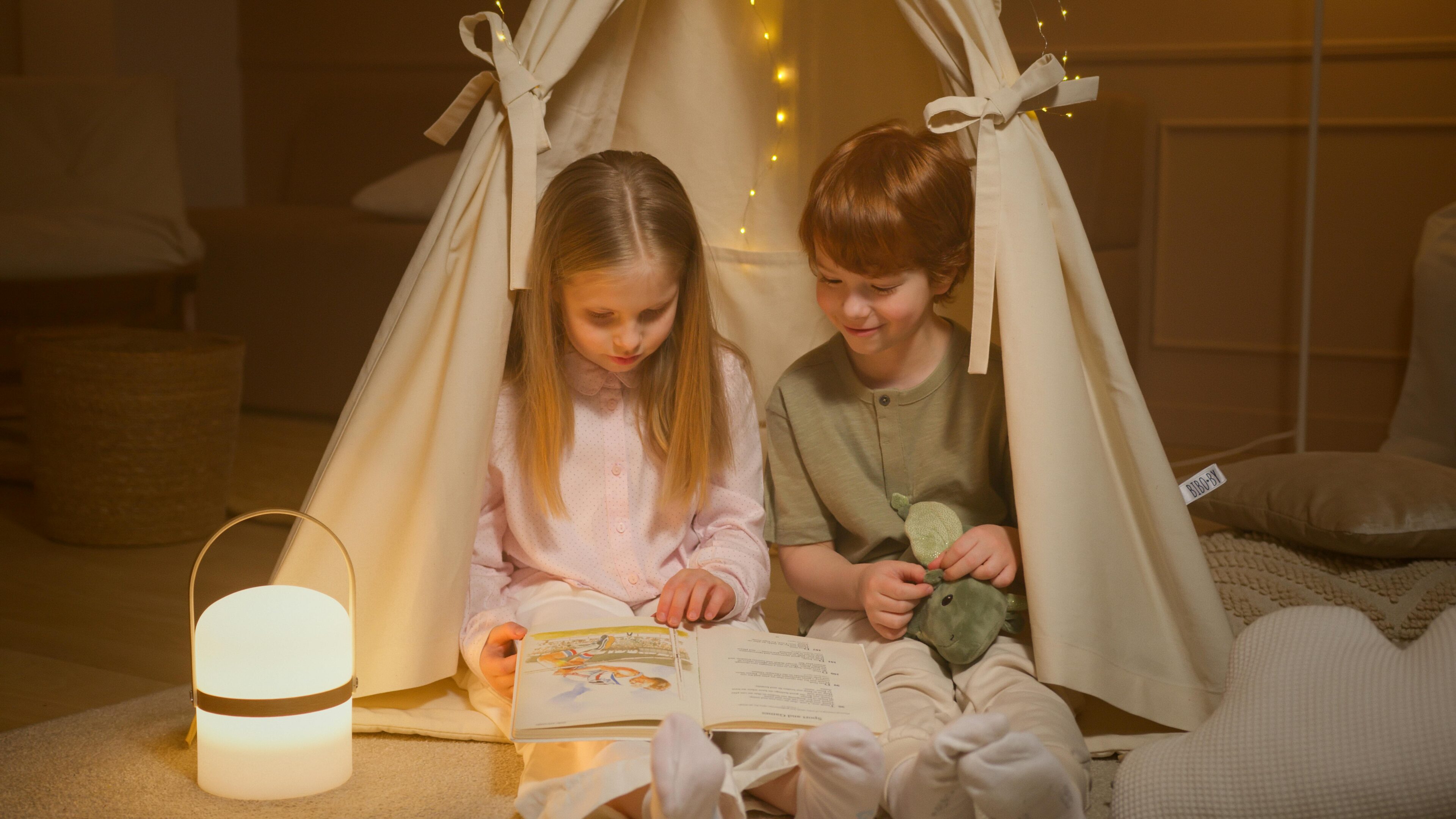 Two children sitting in a teepee reading