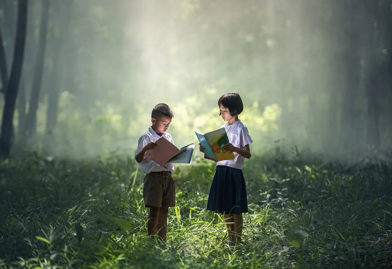 Two children are standing in a field reading books.